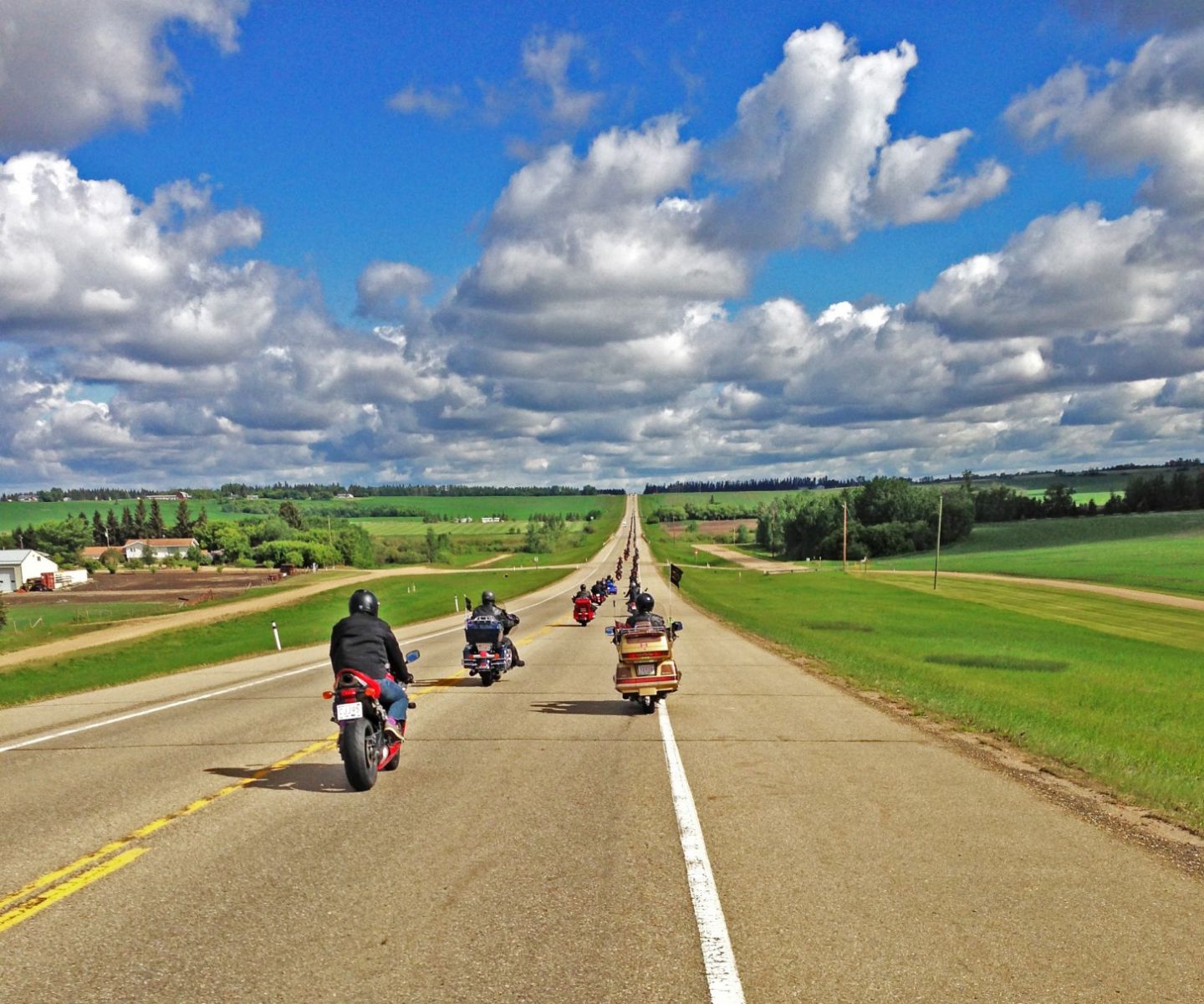 Motociclistas avanzando por una larga carretera de las praderas bajo un cielo amplio durante la Ride for Dad