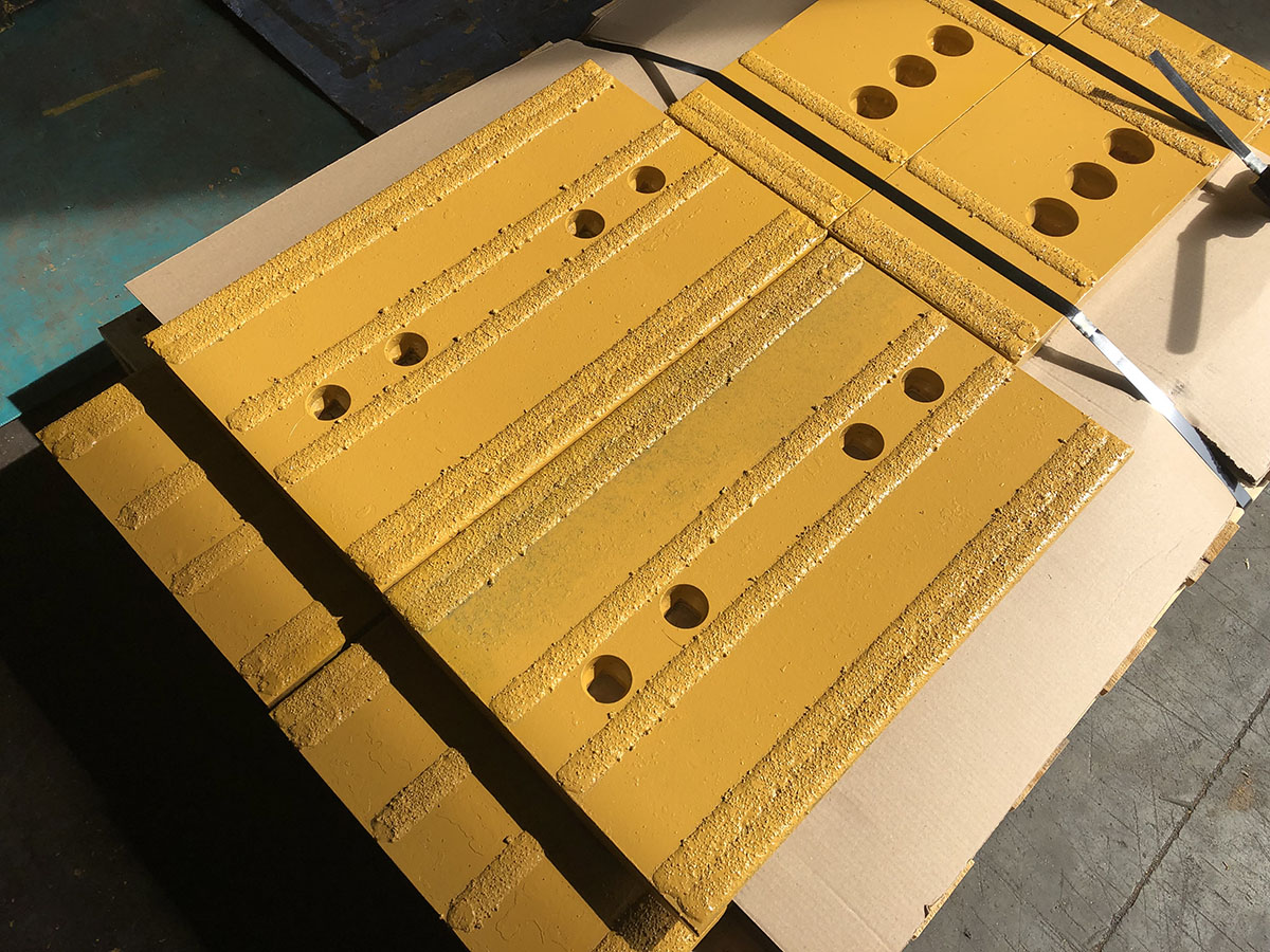 Placas de desgaste pintadas de amarillo con franjas de recubrimiento y orificios para pernos, apiladas sobre una paleta