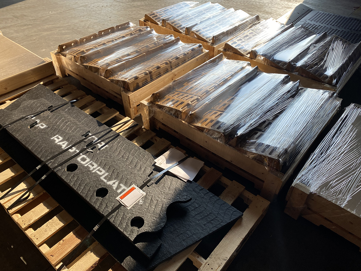 Cajas de madera con piezas de desgaste envueltas en pl&aacute;stico termoencogible y una placa de revestimiento RaptorPlate negra sobre paletas, listas para enviar