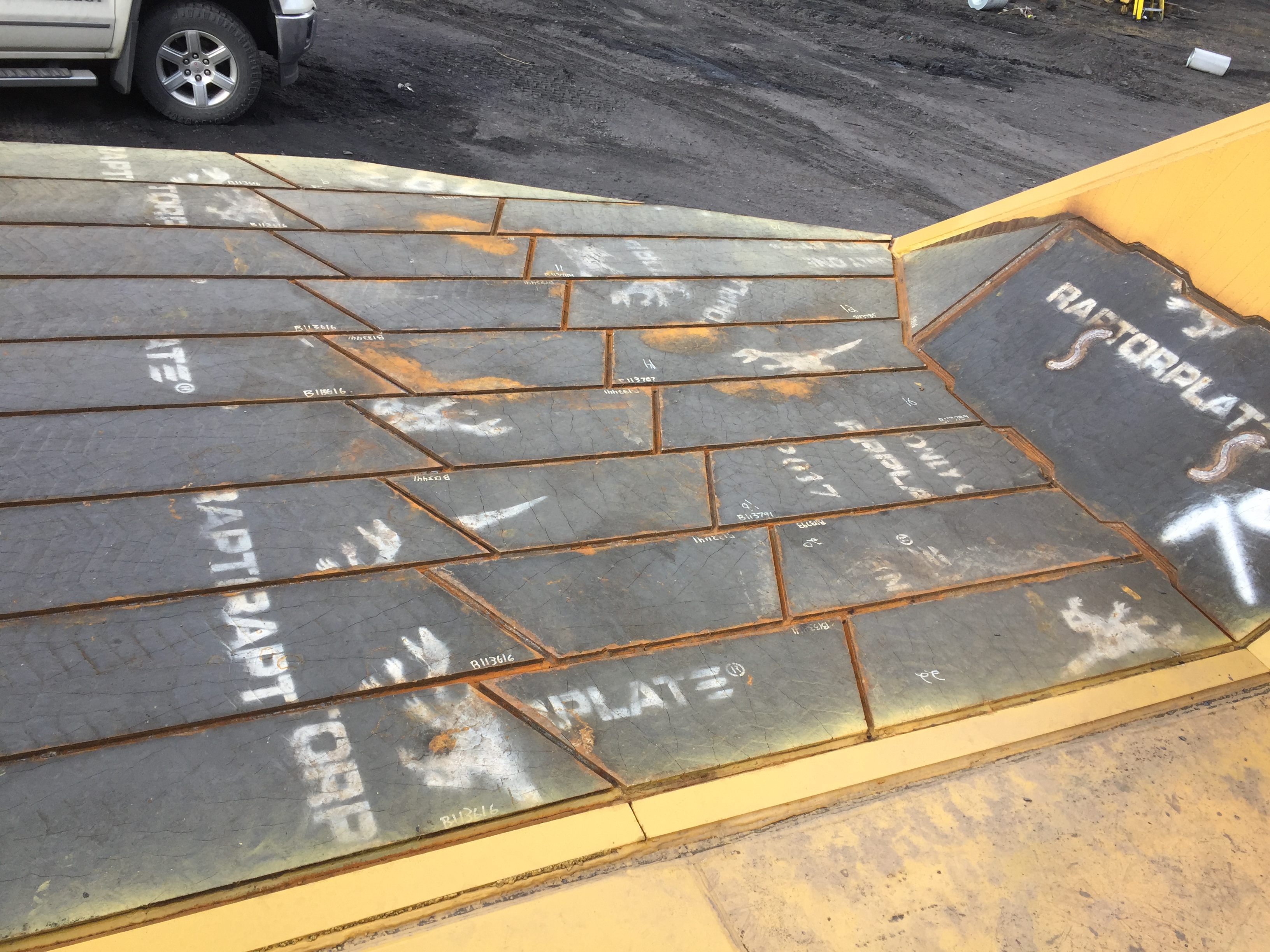 Primer plano de placas de desgaste grises superpuestas que revisten una caja de cami&oacute;n, marcadas con letras y logotipos blancos de RaptorPlate