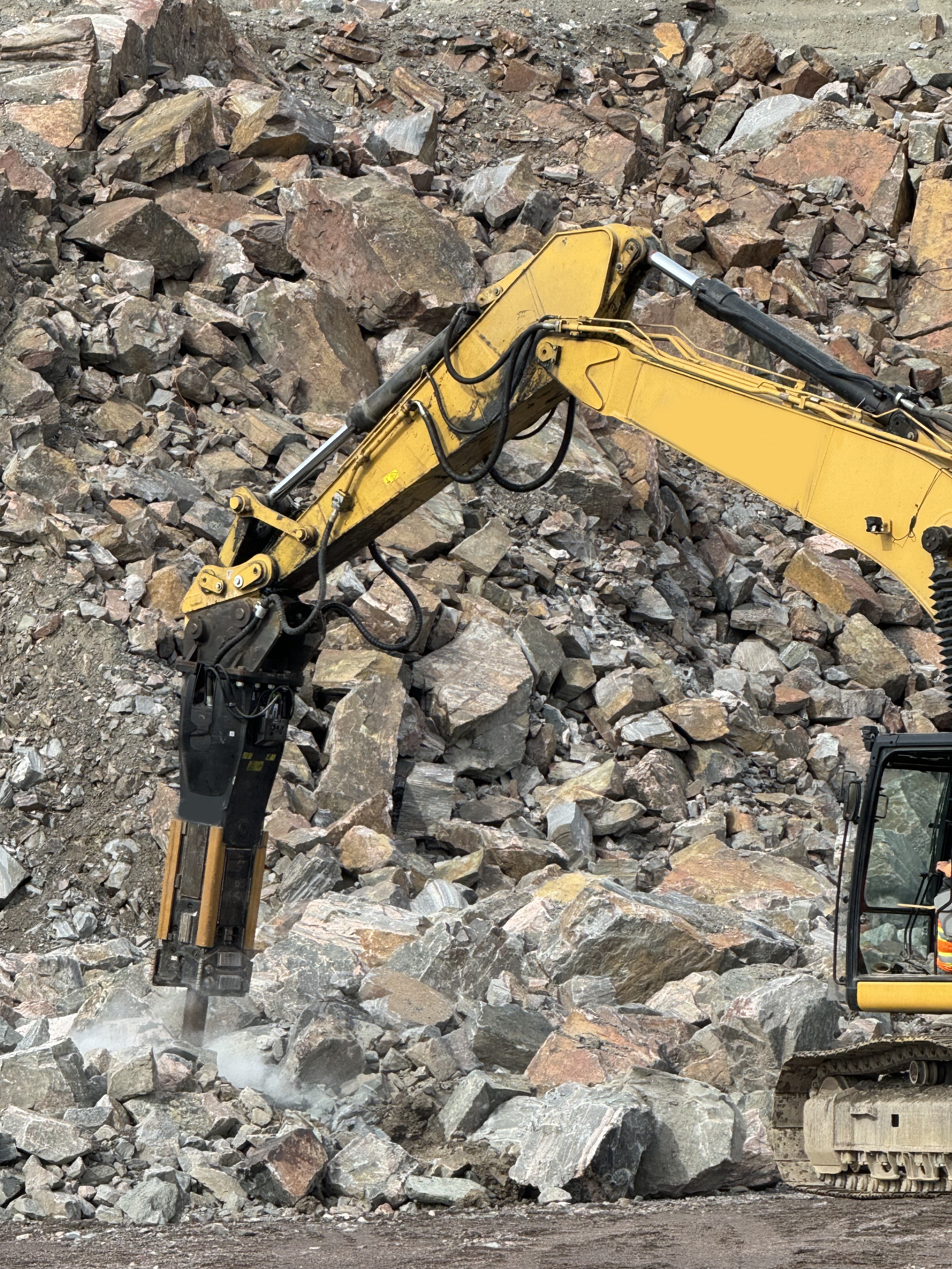 Excavadora amarilla trabajando con un martillo hidr&aacute;ulico sobre una pila de roca fragmentada