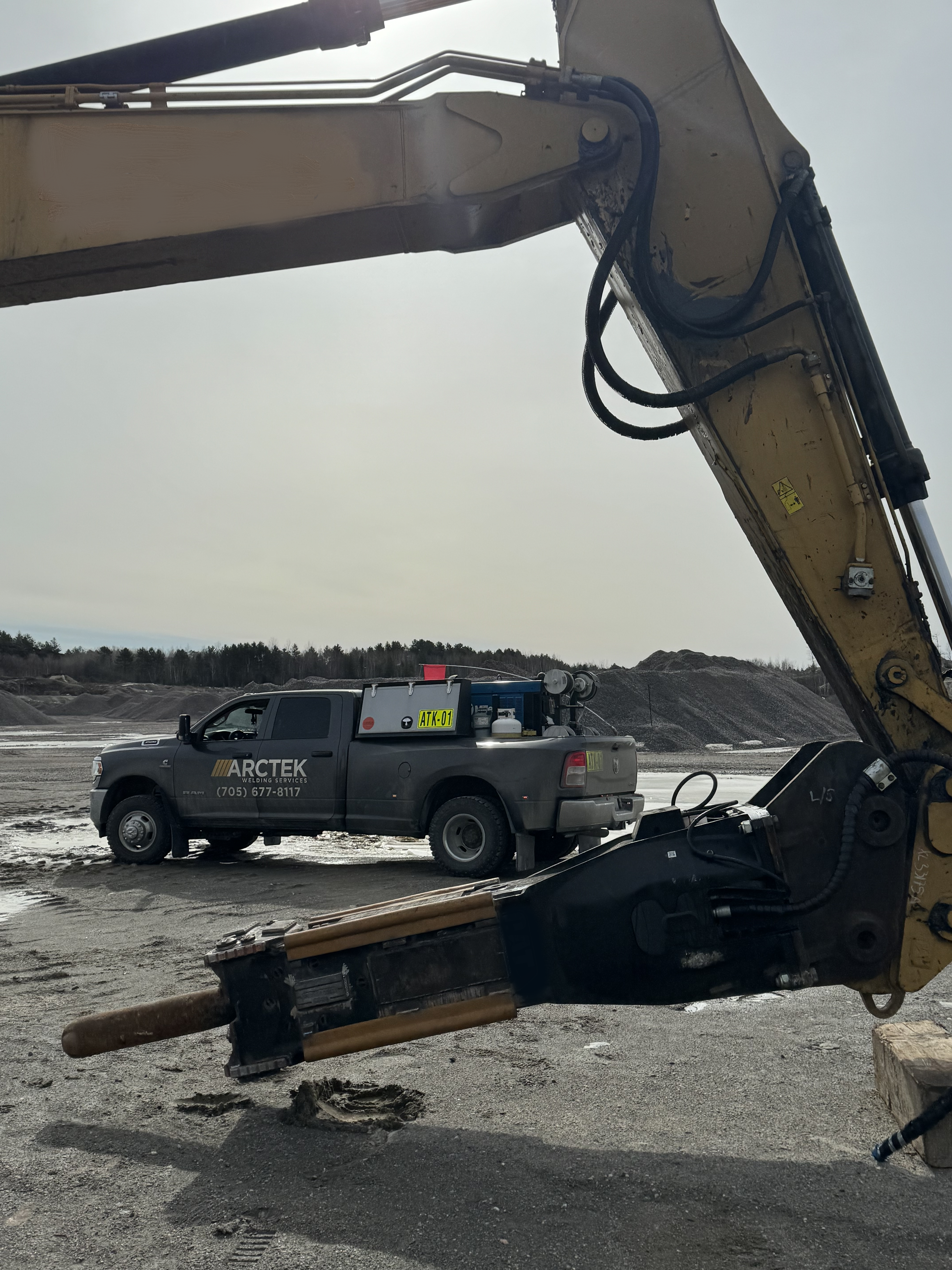 Martillo hidr&aacute;ulico montado en el brazo de una excavadora en una cantera, con un cami&oacute;n de servicio estacionado al fondo