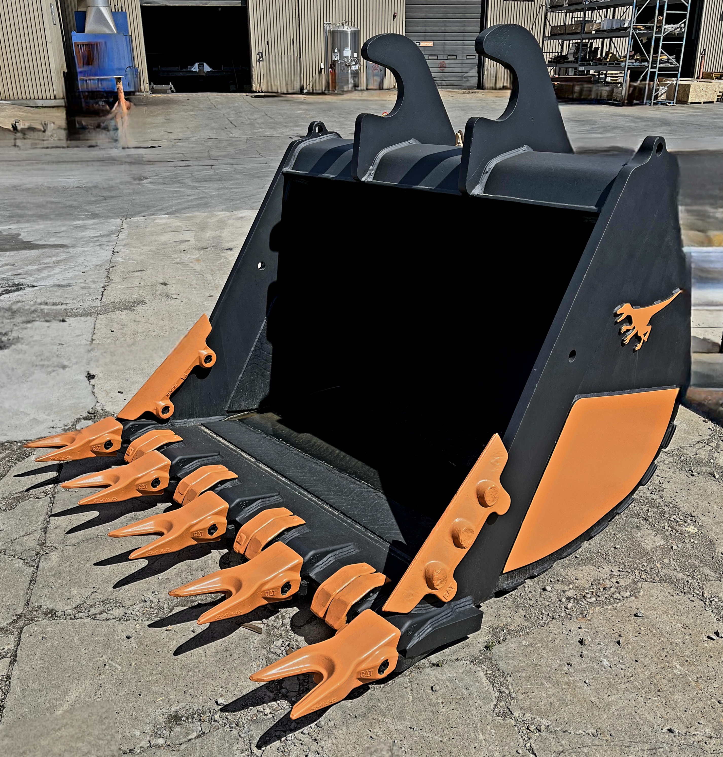 Balde de excavaci&oacute;n Raptor Serie 300 negro con dientes naranjas y protectores laterales, frente a un taller