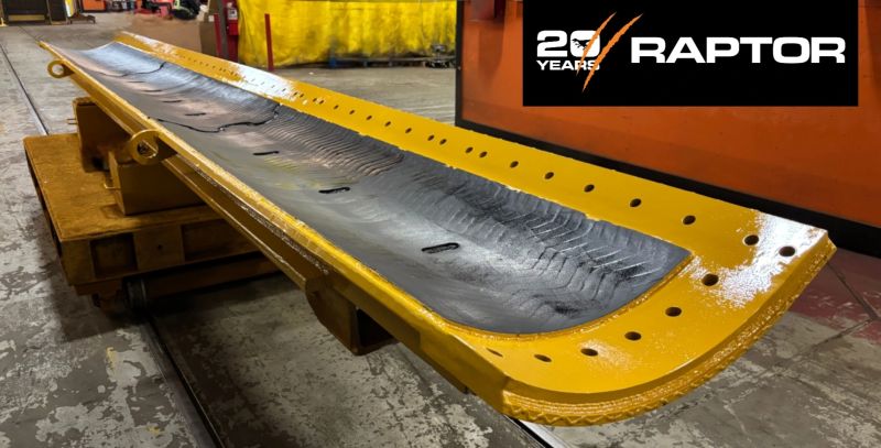 Vertedera larga reparada, pintada de amarillo, con una tira de placa de desgaste negra, sobre un soporte junto al logotipo de Raptor 20 Years
